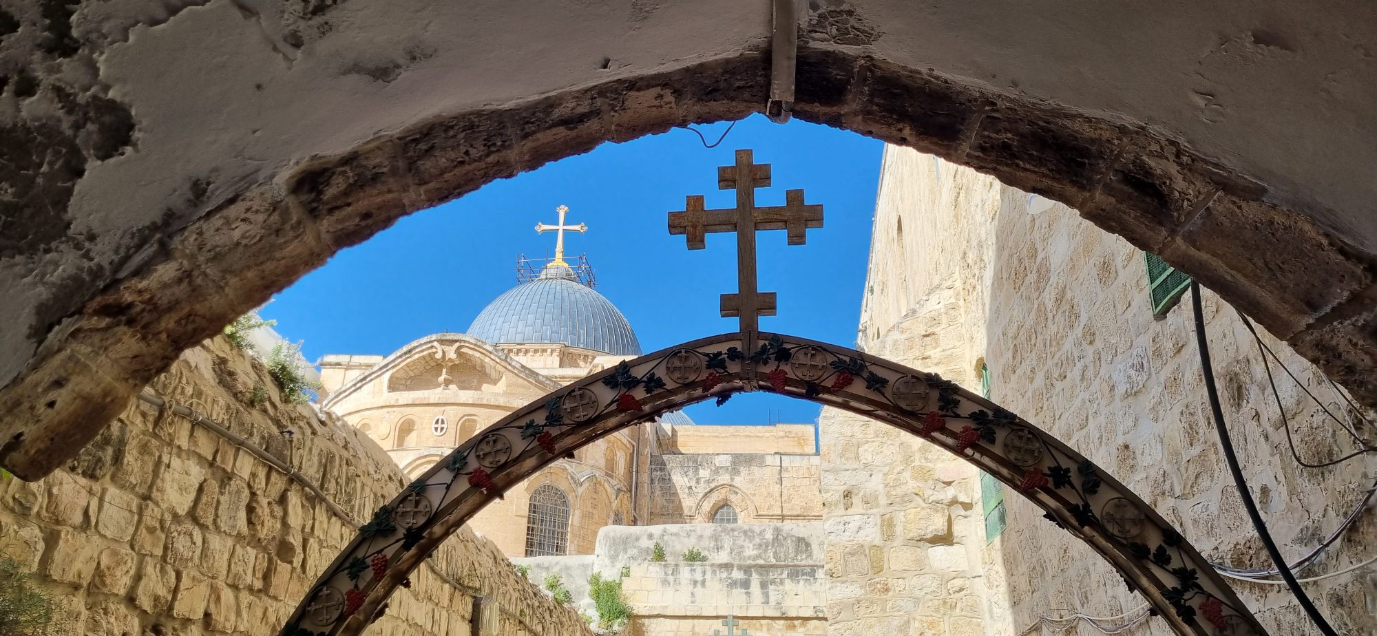 Cruz em primeiro plano em Jerusalém, com a cúpula do Santo Sepulcro ao fundo